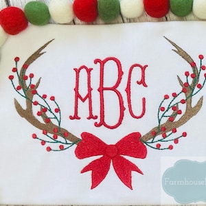 May include: Embroidered Christmas design featuring a red bow, antlers, and red berries with the monogram "ABC" in red.