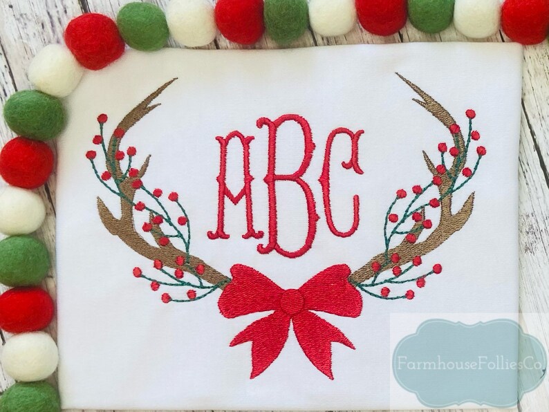 May include: Embroidered Christmas design featuring a red bow, antlers, and red berries with the monogram "ABC" in red.