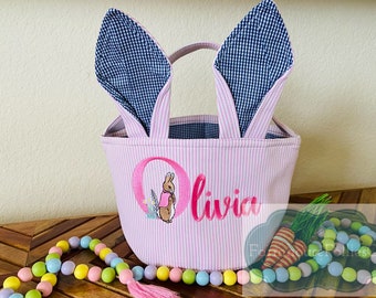 Peut inclure: Panier de Pâques rayé rose et blanc avec des oreilles de lapin. Le panier est brodé d'un lapin rose et du nom "Olivia".