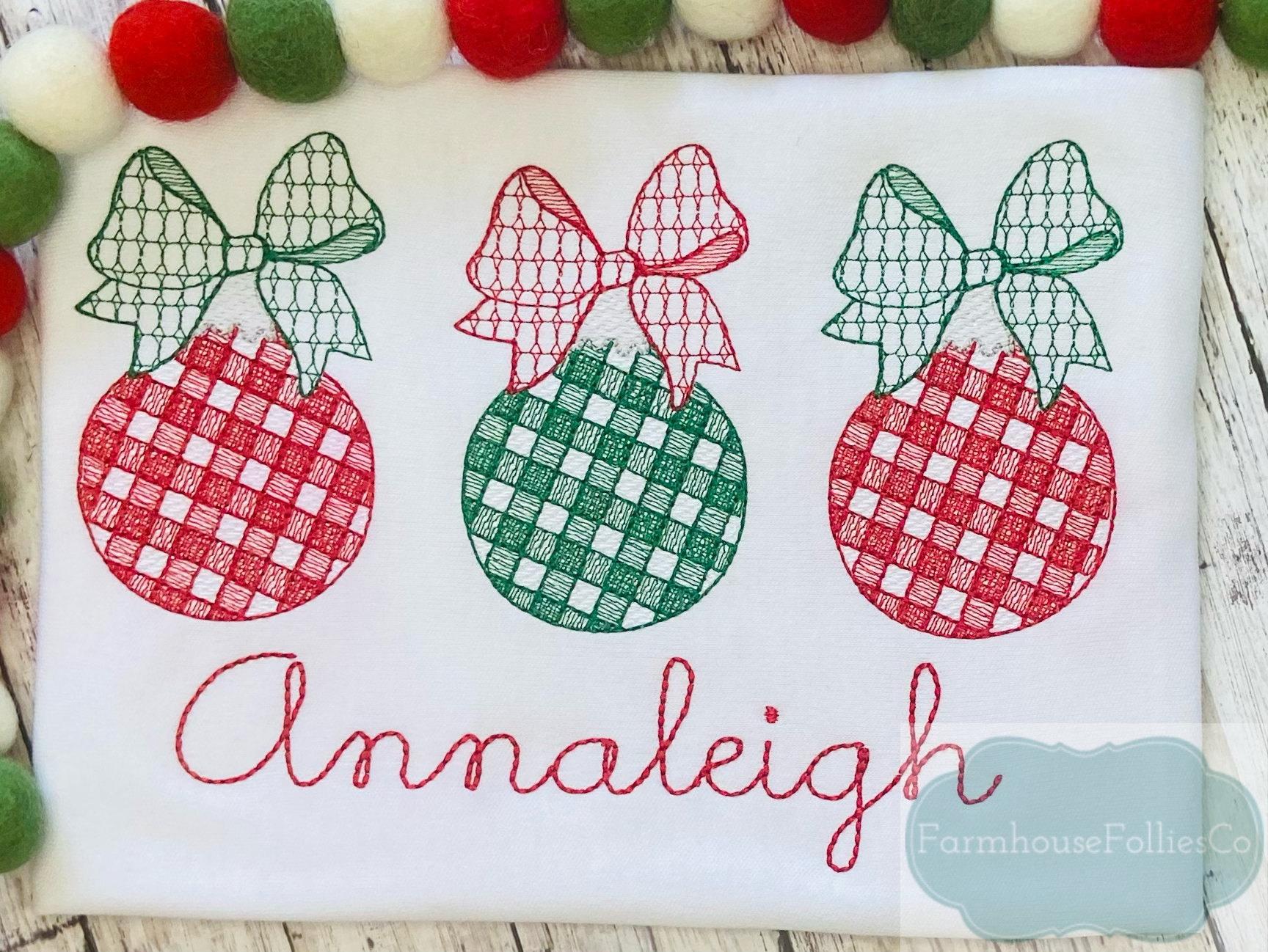 Pode incluir: Tr&ecirc;s enfeites de Natal vermelhos e verdes com la&ccedil;os, bordados em um tecido branco com o nome "Annaleigh" e o texto "Farmhouse Follies Co."