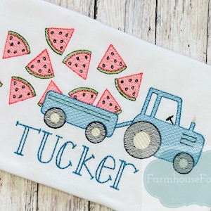 May include: A blue toy tractor with a wagon full of watermelon slices. The tractor is pulling a wagon full of watermelon slices. The word "Tucker" is embroidered below the tractor.