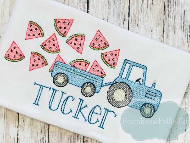 May include: A blue toy tractor with a wagon full of watermelon slices. The tractor is pulling a wagon full of watermelon slices. The word "Tucker" is embroidered below the tractor.