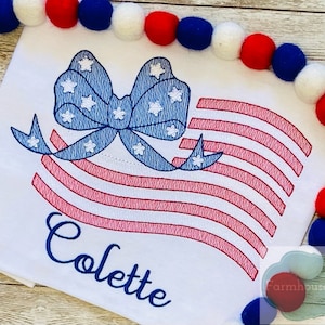 May include: Embroidered design of an American flag with a blue bow and white stars. The name "Colette" is embroidered below the flag.