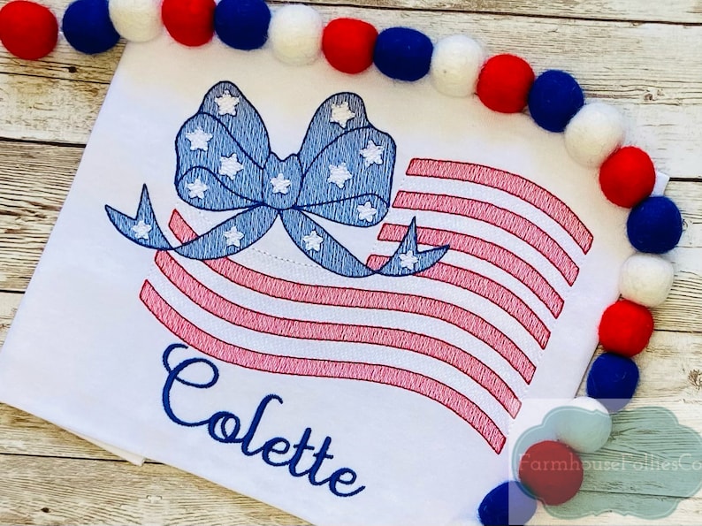 May include: Embroidered design of an American flag with a blue bow and white stars. The name "Colette" is embroidered below the flag.