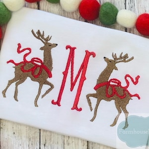 May include: White embroidered Christmas onesie with two red-ribboned reindeer and the letter "M" in red.