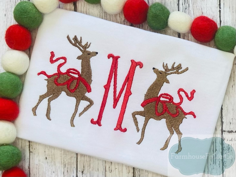 May include: White embroidered Christmas onesie with two red-ribboned reindeer and the letter "M" in red.
