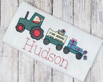 May include: Embroidered design of a green tractor pulling a wagon full of presents. The tractor has a red roof and a red wheel. The wagon is white with a wooden slat design. The text "Hudson" is embroidered below the tractor.
