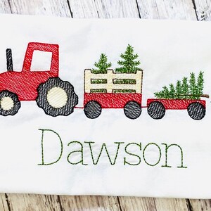 May include: Red toy tractor pulling a wagon with three green Christmas trees. The wagon has a white wooden slatted side. The text "Dawson" is embroidered below the tractor.