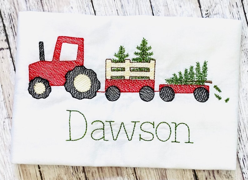 May include: Red toy tractor pulling a wagon with three green Christmas trees. The wagon has a white wooden slatted side. The text "Dawson" is embroidered below the tractor.