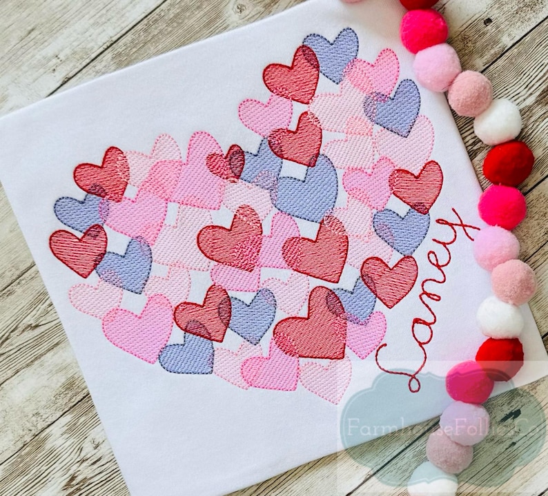 Pu&ograve; includere: Un tessuto bianco con un grande disegno a forma di cuore composto da cuori rosa, rossi e viola. Il nome "Laney" &egrave; ricamato in un font corsivo sotto il cuore.