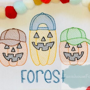 May include: Three embroidered pumpkin faces wearing baseball caps in brown, blue, and green. The pumpkins are orange and have black eyes, noses, and mouths. The text "Forest" is embroidered below the pumpkins.