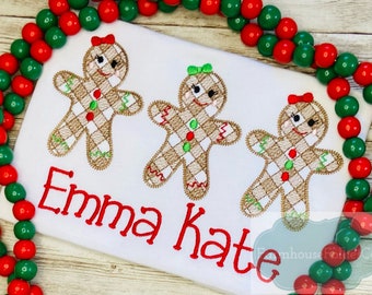 May include: White t-shirt with three embroidered gingerbread people and the names "Emma Kate" in red thread.