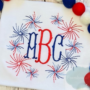 May include: White t-shirt with a red, white and blue embroidered design of fireworks around the letters "ABC".