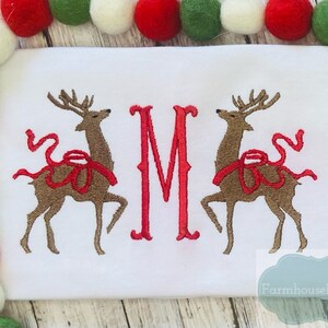 May include: White embroidered Christmas onesie with two red-nosed reindeer and a red letter M. The text "Farmhouse Follies Co." is in the bottom right corner.
