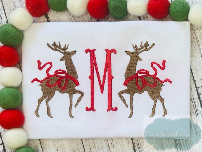May include: White embroidered Christmas onesie with two red-nosed reindeer and a red letter M. The text "Farmhouse Follies Co." is in the bottom right corner.