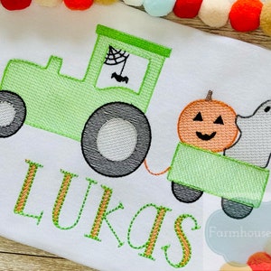 Op de afbeelding: Groene tractor met een pompoen en een spook in de wagen. De tractor heeft een spinnenweb en een vleermuis in het raam. De naam "LUKAS" is geborduurd onder de tractor.