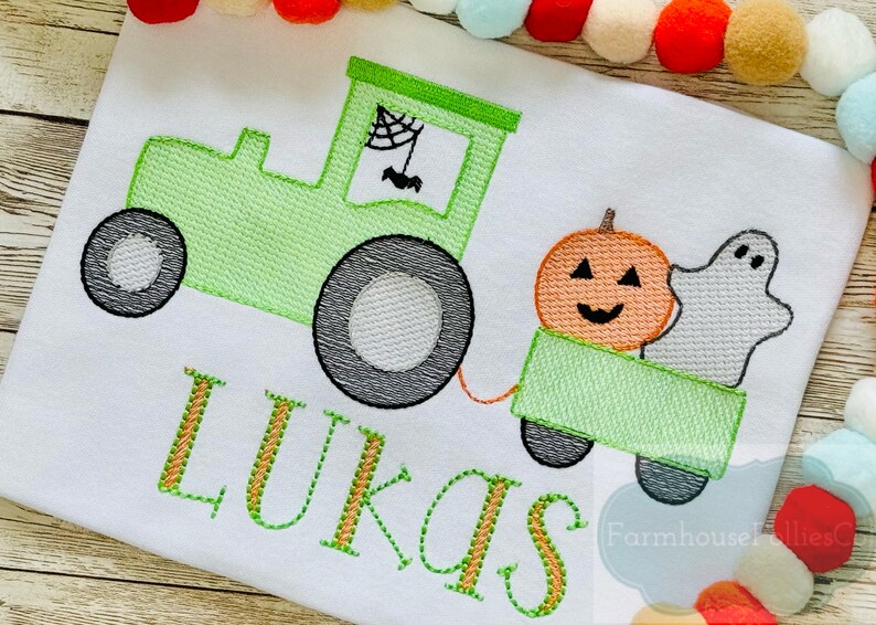 Op de afbeelding: Groene tractor met een pompoen en een spook in de wagen. De tractor heeft een spinnenweb en een vleermuis in het raam. De naam "LUKAS" is geborduurd onder de tractor.