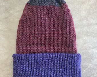 May include: A knitted beanie hat in three colors: dark blue at the top, burgundy in the middle, and a deep purple at the brim. The hat is made of a soft, textured yarn.