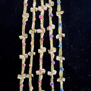 Puede incluir: Cinco hebras de ribete dorado con pequeños lazos y detalles de flores de colores. El ribete es perfecto para agregar un toque de elegancia a cualquier proyecto.