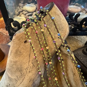 Op de afbeelding: Vijf strengen bruine, groene en witte trim met kleine gekleurde bloemen. De trim is om een ​​houten schoenleest gewikkeld.