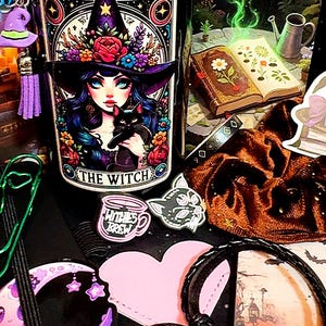 May include: A black jar with a decorative label featuring a witch with blue hair and a black cat. The label reads "THE WITCH". The image includes charms, stickers, and a bracelet, all with a witchy theme.