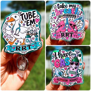 May include: Three glittery acrylic badge reels featuring respiratory therapy themes. One shows a duck with medical equipment and the text TUBE EM RRT. Another depicts lungs with microphones and the text take my breath awayyyyy RRT. The third shows an oxygen tank with the text I HAVE GAS RESPIRATORY THERAPIST.