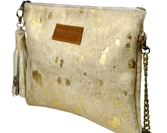 Könnte beinhalten: Eine kleine, cremefarbene Clutch mit einer goldenen Kettenkette und einem goldenen Quastenanhänger. Die Tasche hat einen braunen Lederfleck mit dem Text "SWAN TURFED" in goldenen Buchstaben.