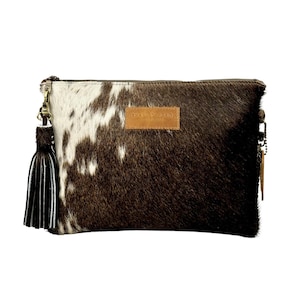 K&ouml;nnte beinhalten: Eine braune und wei&szlig;e Clutch aus Kuhfell mit einem braunen Leder-Quaste und einem braunen Leder-Etikett mit der Aufschrift "CHAND TWEED".