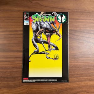 Puede incluir: Portada de cómic "SPAWN" con título verde y amarillo. La ilustración muestra un monstruo con garras y cuernos sobre fondo amarillo. El cómic está marcado con "1" y tiene una advertencia sobre piezas pequeñas. Número de artículo 10004.