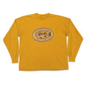 Puede incluir: Camiseta de manga larga de color amarillo mostaza con un gr&aacute;fico en la parte delantera. El gr&aacute;fico es un dise&ntilde;o ovalado con una ilustraci&oacute;n de pez y las palabras "WINNECONNE WISCONSIN" y "A SMALL DRINKING VILLAGE WITH A BIG FISHING PROBLEM".
