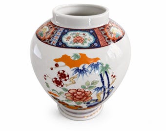 Peut inclure: Un vase en céramique blanche avec un corps arrondi et une base évasée. Le bord supérieur présente une bande décorative de motifs géométriques et floraux en rouge, bleu et or. Le corps affiche des motifs peints de fleurs et de bambous.