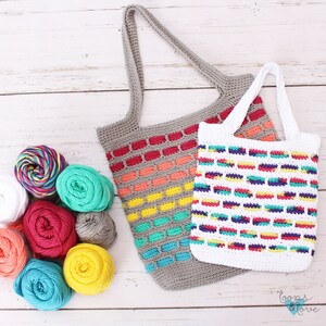 May include: Two crocheted bags with colorful striped patterns. The larger bag is gray with red, orange, yellow, green, and blue stripes. The smaller bag is white with red, yellow, green, blue, and purple stripes. Both bags have crocheted handles.
