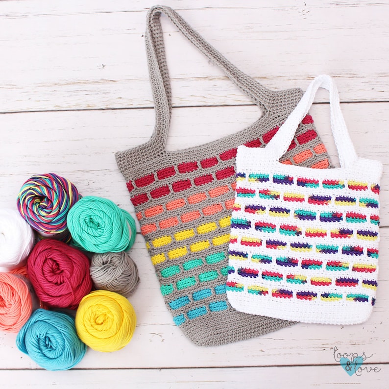 May include: Two crocheted bags with colorful striped patterns. The larger bag is gray with red, orange, yellow, green, and blue stripes. The smaller bag is white with red, yellow, green, blue, and purple stripes. Both bags have crocheted handles.