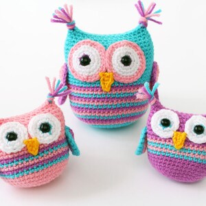 May include: Three crocheted owl plushies in different sizes. The largest owl is turquoise with pink and purple stripes. The medium owl is pink with purple and turquoise stripes. The smallest owl is purple with turquoise and pink stripes.