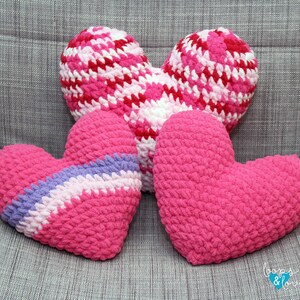 May include: Three crocheted heart-shaped pillows in pink, white, and purple. The pillows are arranged on a gray fabric surface. The text "Loops & Love" is visible in the bottom right corner of the image.