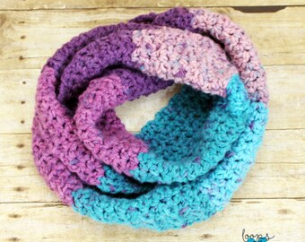 May include: A crocheted infinity scarf in shades of purple, pink, and teal. The scarf is made with a chunky yarn and has a simple stitch pattern.