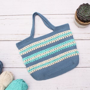 May include: A blue crocheted tote bag with white and turquoise stripes. The bag has a wide, flat base and two handles.
