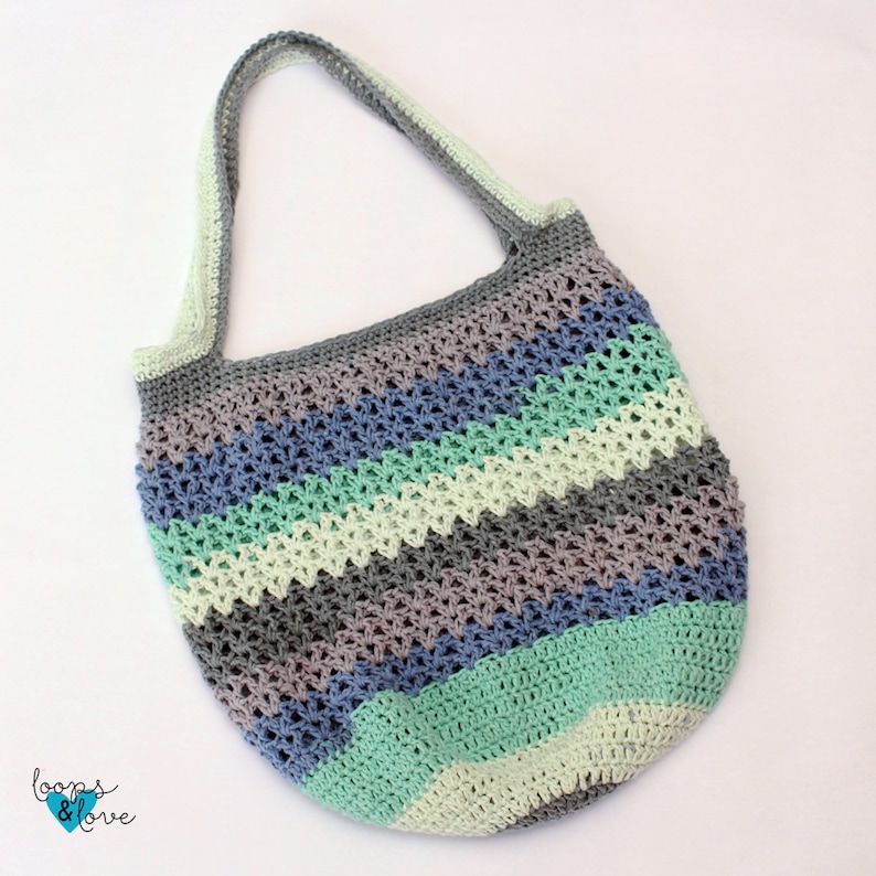 May include: A crocheted tote bag with a striped pattern in shades of gray, blue, green, and cream. The bag has a single long strap.