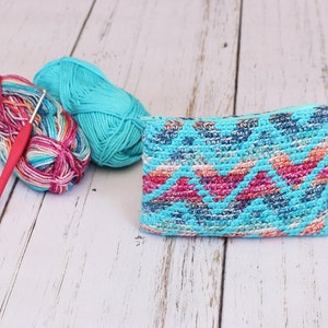 Puede incluir: Una bolsa de crochet turquesa con un patr&oacute;n geom&eacute;trico colorido, dos ovillos de lana y un ganchillo.