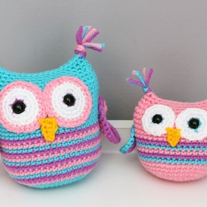 May include: Two crocheted owls, one pink and one blue, with pink and purple stripes. Both owls have white eyes with black pupils and yellow beaks.