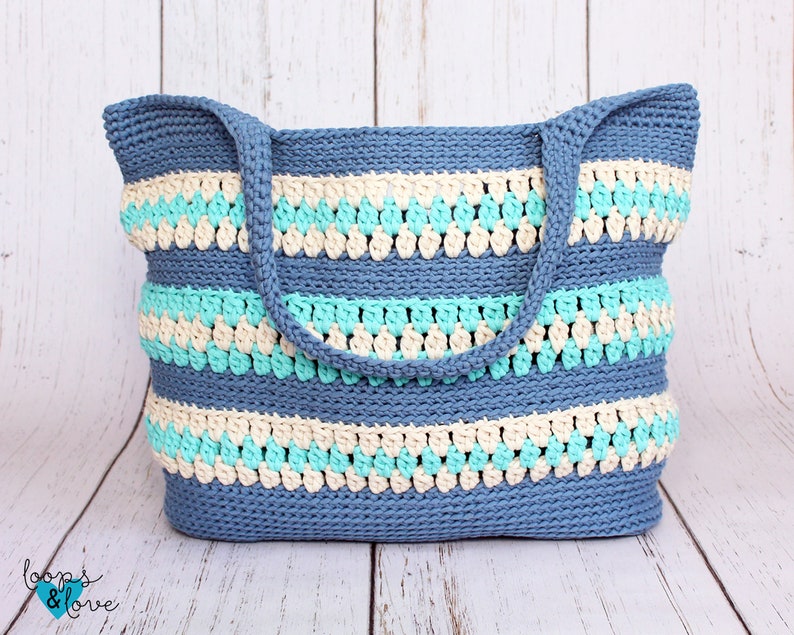 May include: A blue, beige, and turquoise crocheted tote bag with a striped pattern. The bag has two handles.
