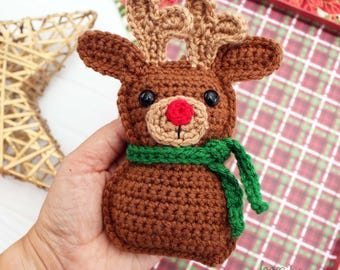 May include: A handmade crochet reindeer ornament with brown body, antlers, and a green scarf. The reindeer has a red nose and black eyes. The ornament is designed for Christmas and holiday decor.