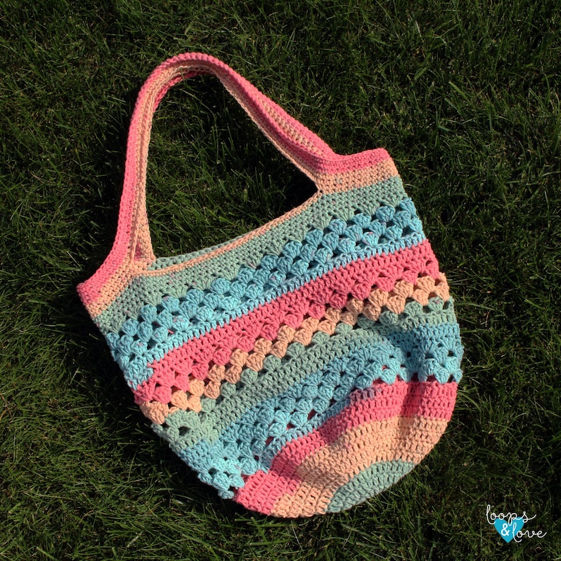 May include: A crocheted tote bag with a striped pattern in pink, blue and beige. The bag has a single handle and is made with a textured stitch.