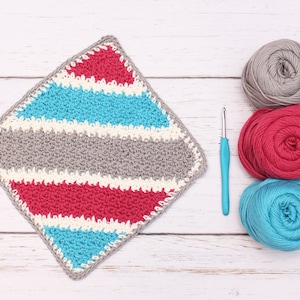 May include: A crocheted square dishcloth with stripes of gray, white, pink, and blue yarn. Three balls of yarn in gray, pink, and blue are next to a blue crochet hook.