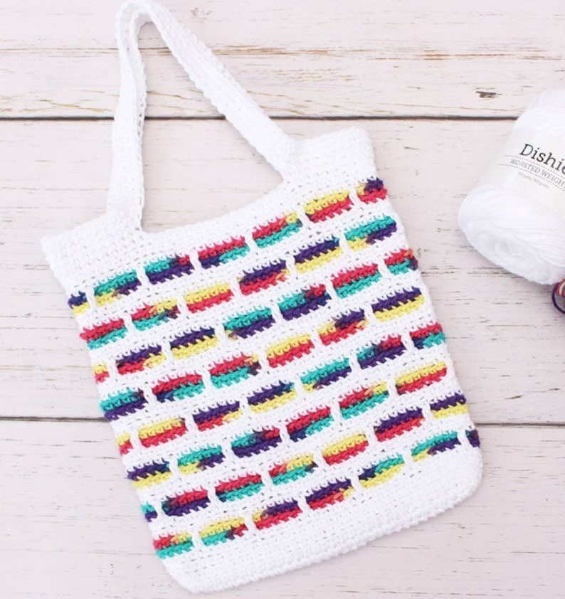 May include: White crochet tote bag with colorful stripes. The bag has a single handle and is made with a simple stitch pattern.