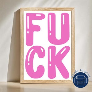 May include: A framed print featuring the word "FUCK" in large, bubble-style, pink letters on a white background. The print is in a light-coloured wooden frame. A blue and white "Ready to print" icon is in the bottom right corner.