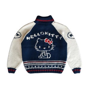May include: A navy blue and cream-coloured knitted sweater featuring a Hello Kitty design. The sweater has a high collar with red trim, cream-coloured sleeves, and a Hello Kitty graphic on the back with the words "HELLO KITTY".