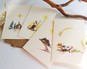 Puede incluir: Conjunto de cuatro tarjetas de Navidad vintage con ilustraciones de acuarela de la escena de la Natividad. Las tarjetas presentan una estrella, un pastor, un pesebre y un establo.