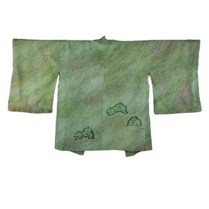 Peut inclure: Un kimono vert avec un motif texturé et trois motifs d'arbres brodés. Le kimono a de larges manches et est posé à plat sur un fond blanc. La couleur est un mélange de vert et de marron clair.