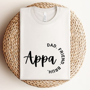 May include: White t-shirt with black text that reads "Appa" in a script font. The text is surrounded by a circle with the words "Dad, Friend,  Bruh" written around it.